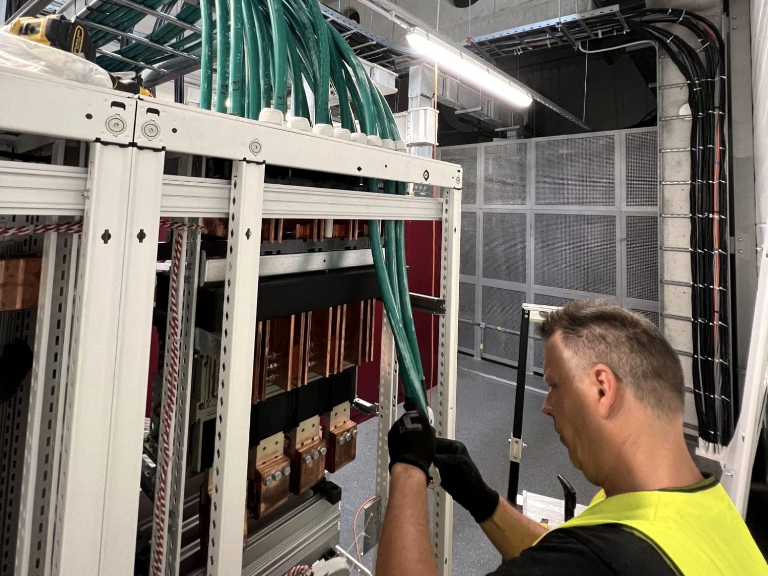 Elektriker schließt Starkstromkabel an eine NS-Hauptverteilung mit Kupferschienen an